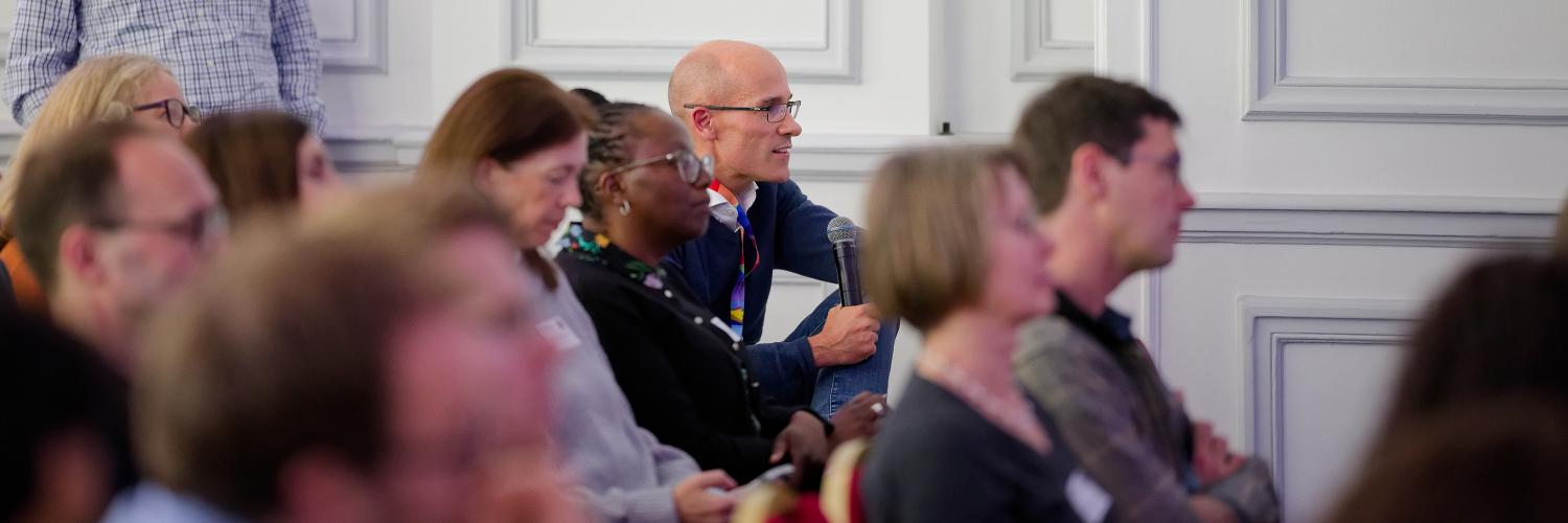 A person with a microphone asking a question in a seated crowd.