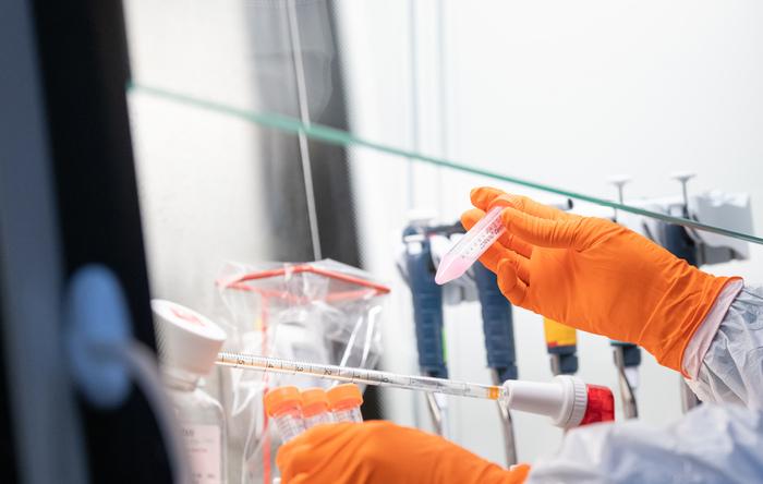 Hands wearing orange gloves handling test tubes in a fume hood.