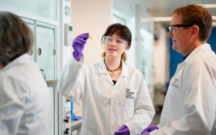 Three people wear lab coats and talk to each other in a lab