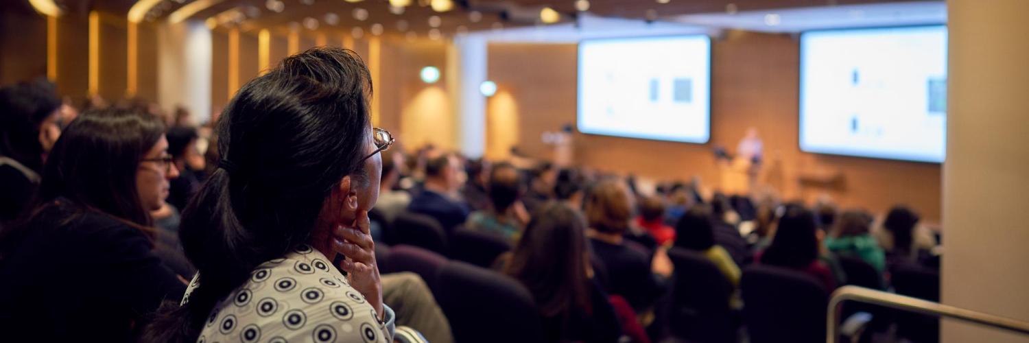 Two women in the foreground and a crowd look at some screens in the Crick auditorium