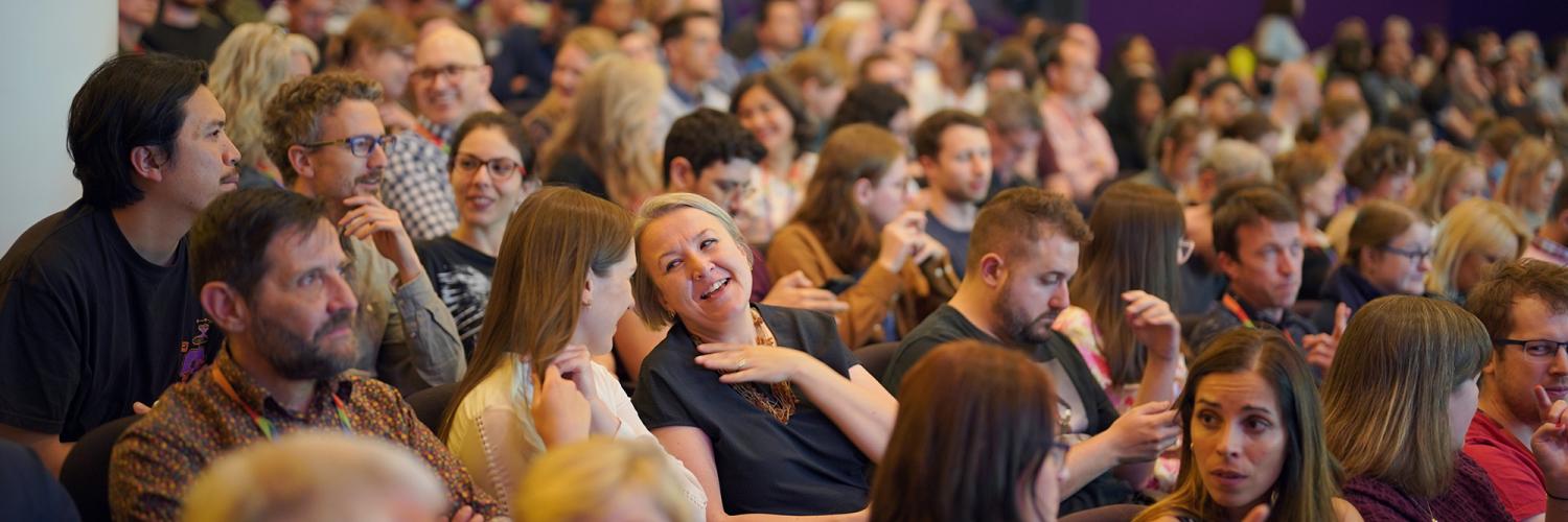 People sit in a lecture theatre and are talking to each other as they wait for it to begin