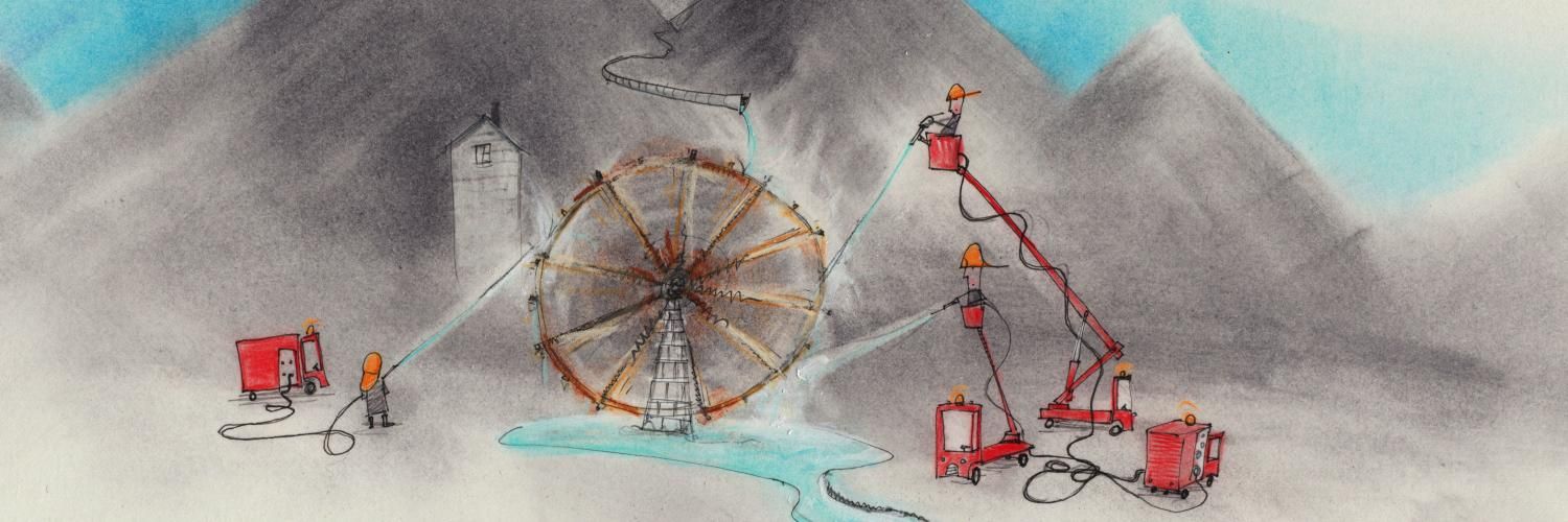 People on extended cranes spraying water on a water wheel, with mountains in the background and a river in the foreground