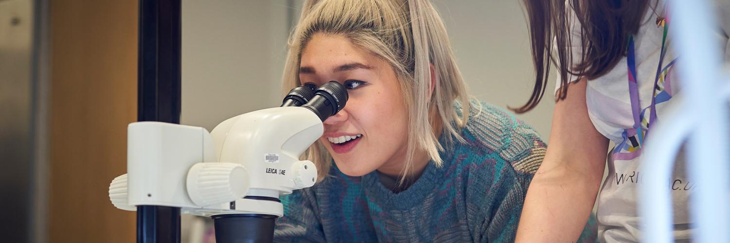 A woman looks with wonder through a microscope