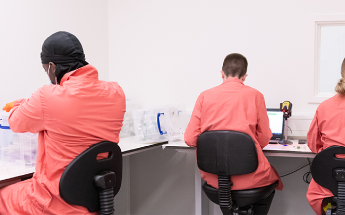 Three people in orange lab coast in a lab with their backs to the camera