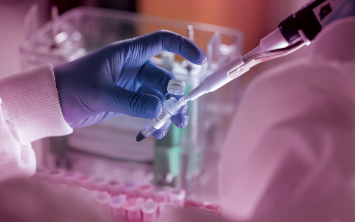 A gloved hand fills a test tube with a pipette