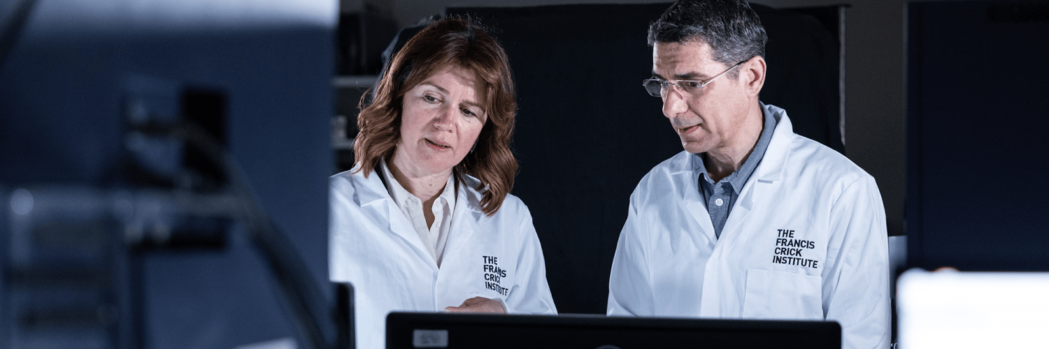 Two people in lab coats look at a screen together in a lab