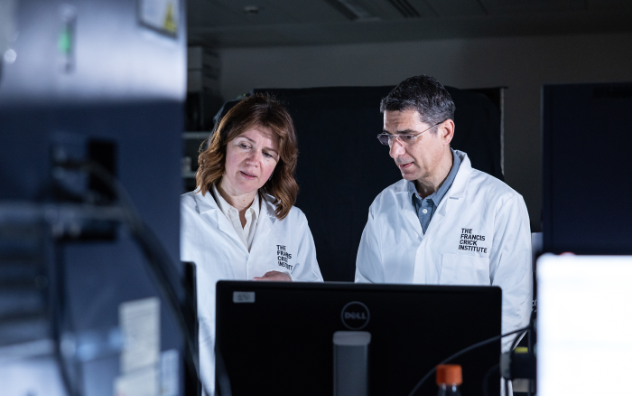 Two people in lab coats look at a screen together in a lab